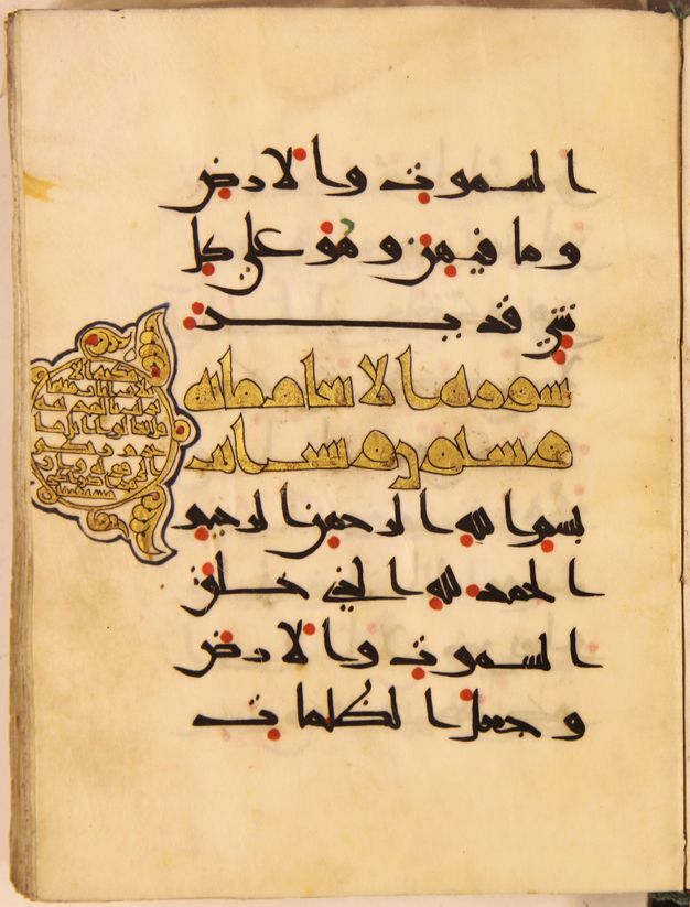 Manuscript page with black Arabic script, red dots, two central lines of golden script, and a golden medallion on the left.