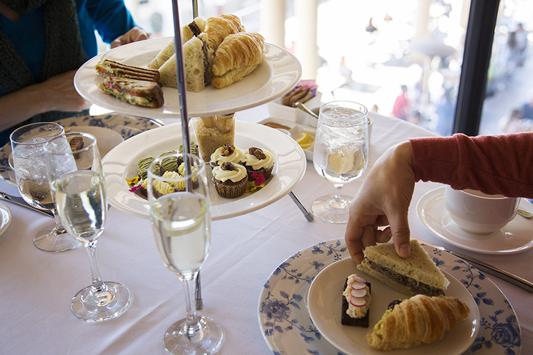 Two people enjoy finger sandwiches and glasses of prosecco at a table overlooking the Getty Villa.