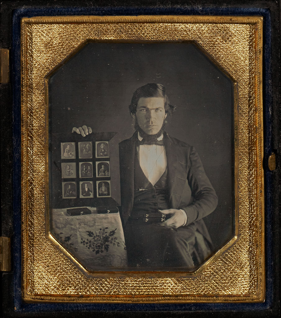 Portrait of a Daguerreotypist Displaying Daguerreotypes and Cases