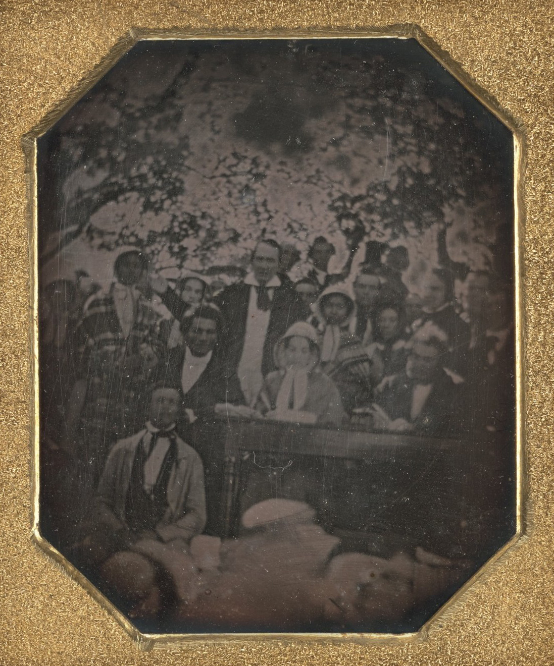 A grainy black and white photograph of a gathering of Black Americans all facing the camera with a gold border around the photograph