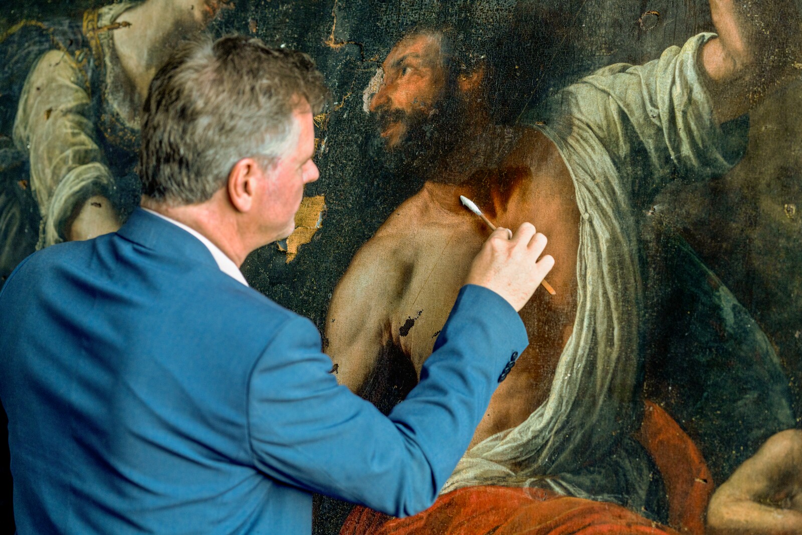 A man in a blue blazer swabs a badly damaged painting