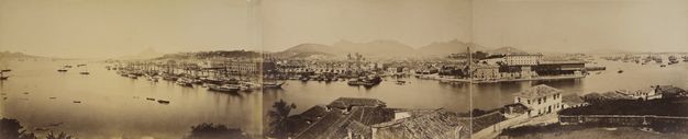 Horizontal, sepia-toned photographic print with two folds, showing rooftops in the foreground and the city, boats, and Carioca hills beyond.