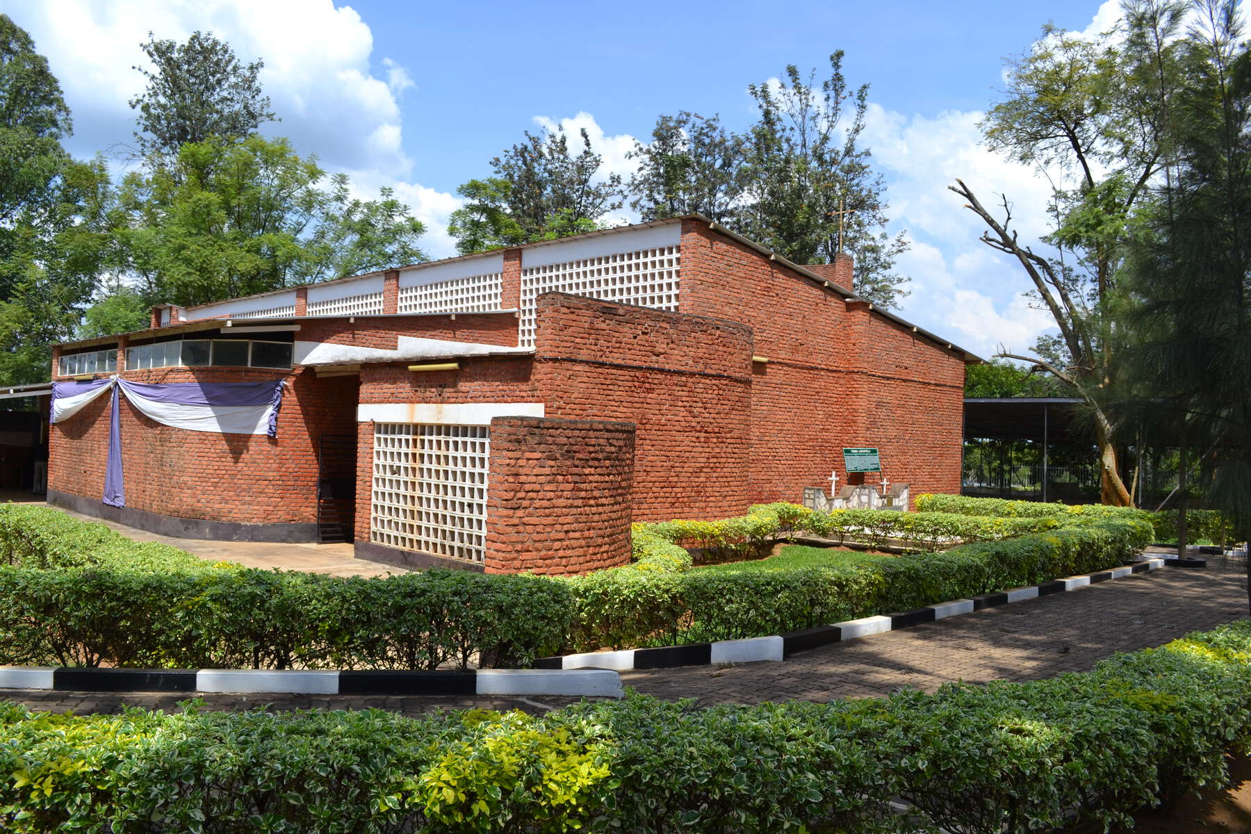 Stained brick building with white panels in the front and on the side, a small stone memorial with two crosses.