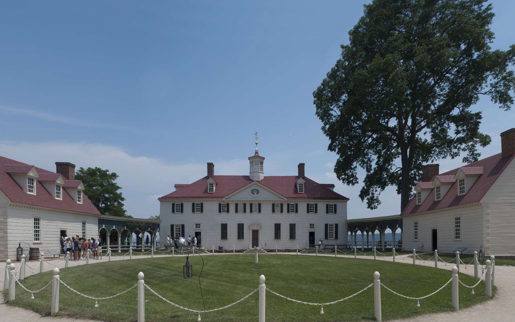 Circular pathway in front of a two-story mansion that has arched hallways connecting to a separate room on each side.