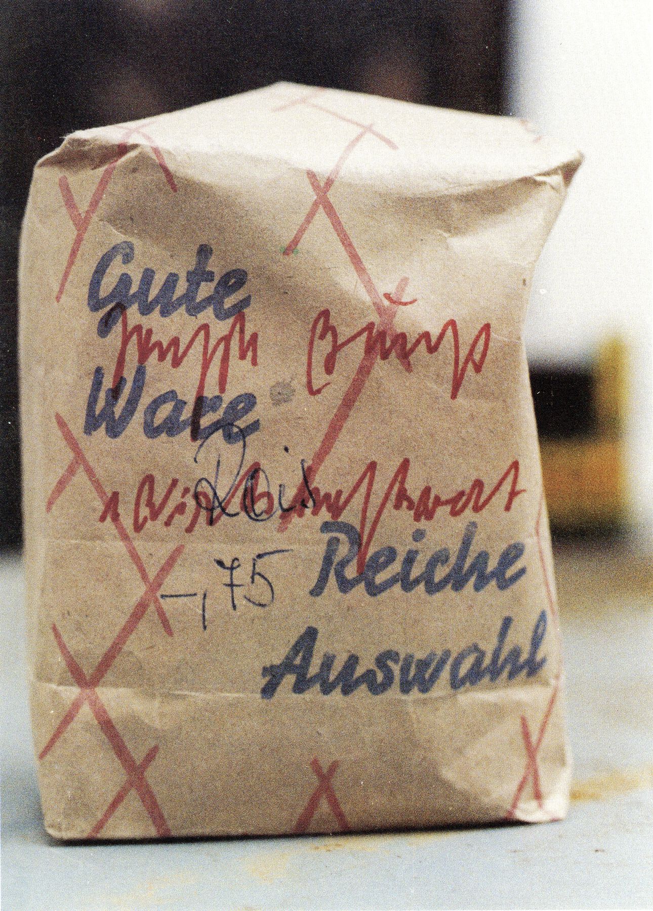 Brown paper bag with red Xs overwritten with blue and red text reading ‘Gute Ware Reiche Auswahl’