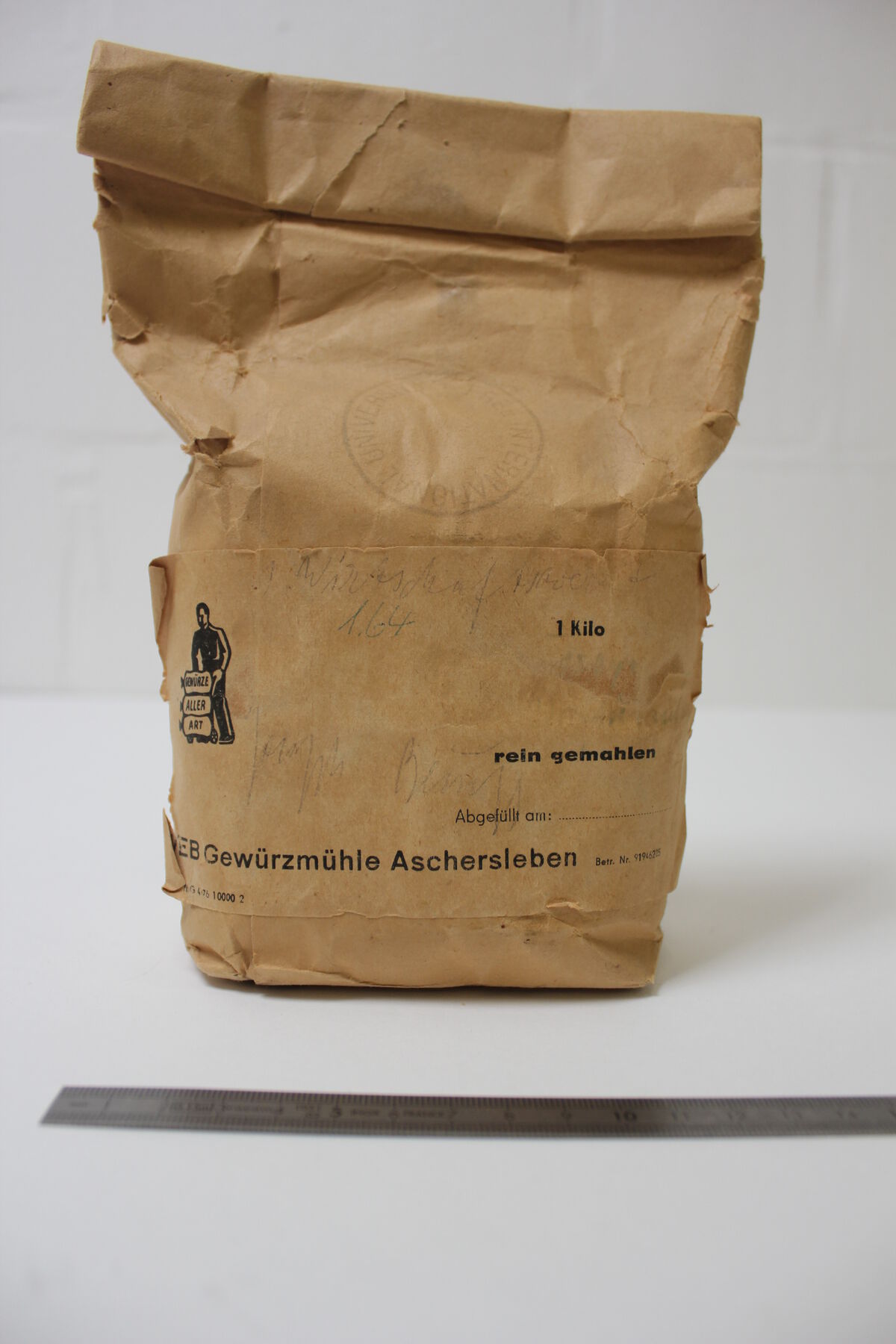 Reddish-brown rolled-up 1-Kilo paper bag with faded stamp and printed words; in front is a metal ruler