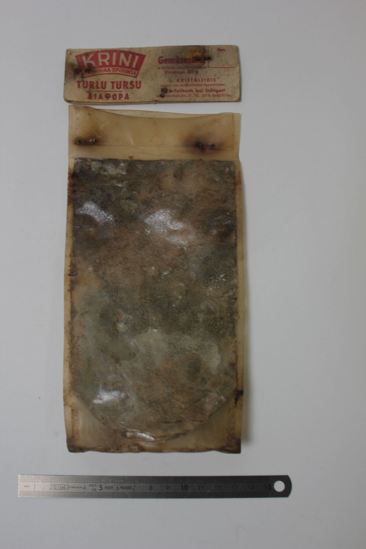 Brownish-green discolored pouch with ‘Krini Turlu Tursu’ label at the top and metal ruler below