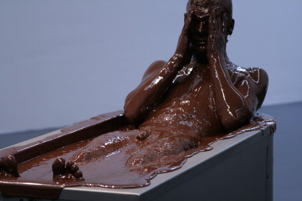 Artist Sonja Alhäuser laying in a stainless-steel bathtub drenched in raw chocolate