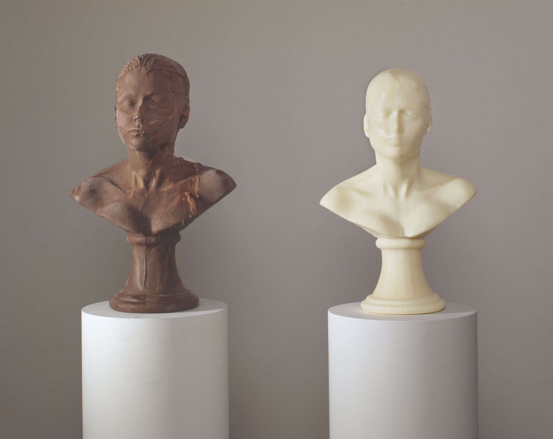 A head bust sculpture made from chocolate displayed next to a head bust made of white soap