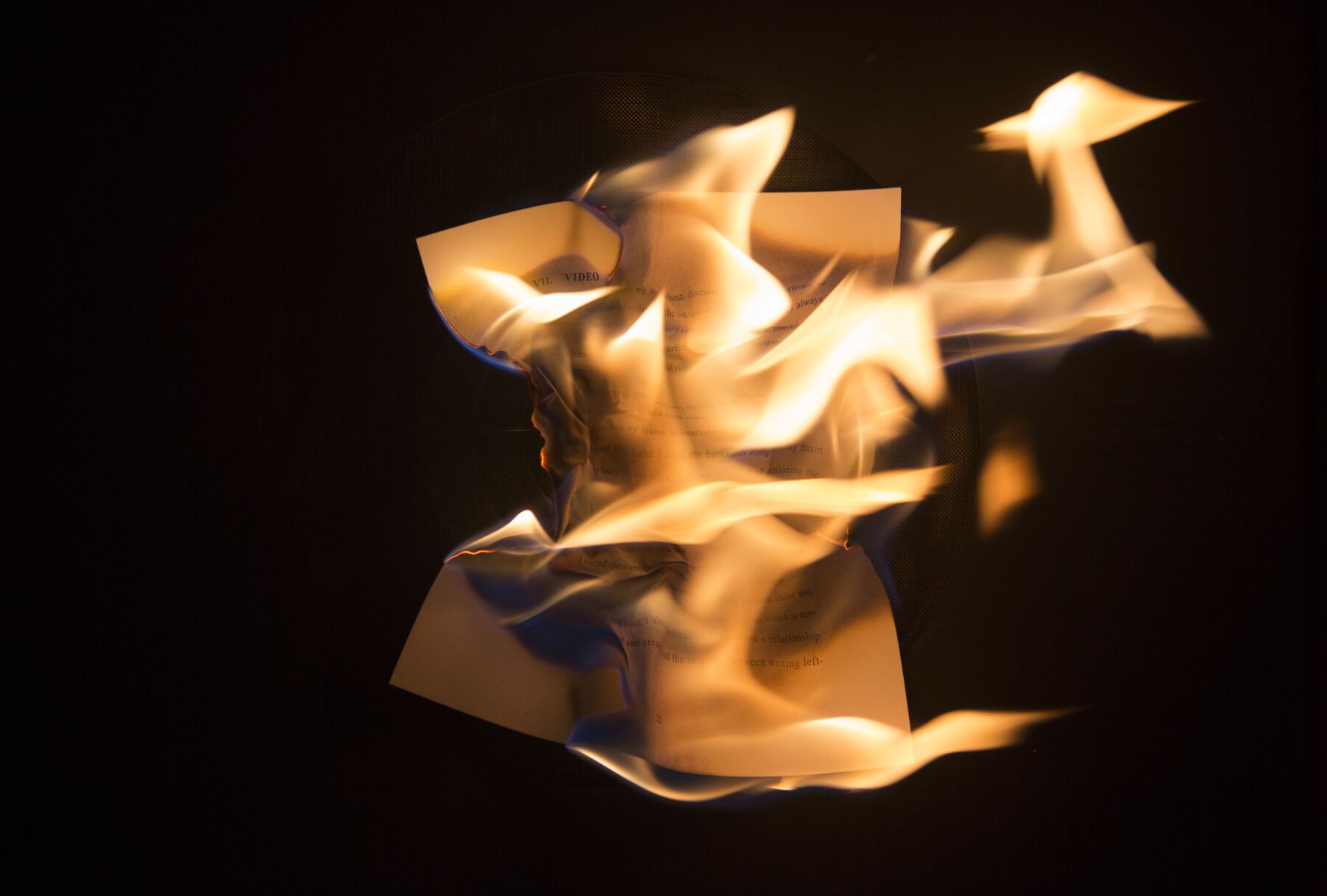 Burning paper with orange flames springing out from printed sheet and electric-blue and fiery-red streaks on left side