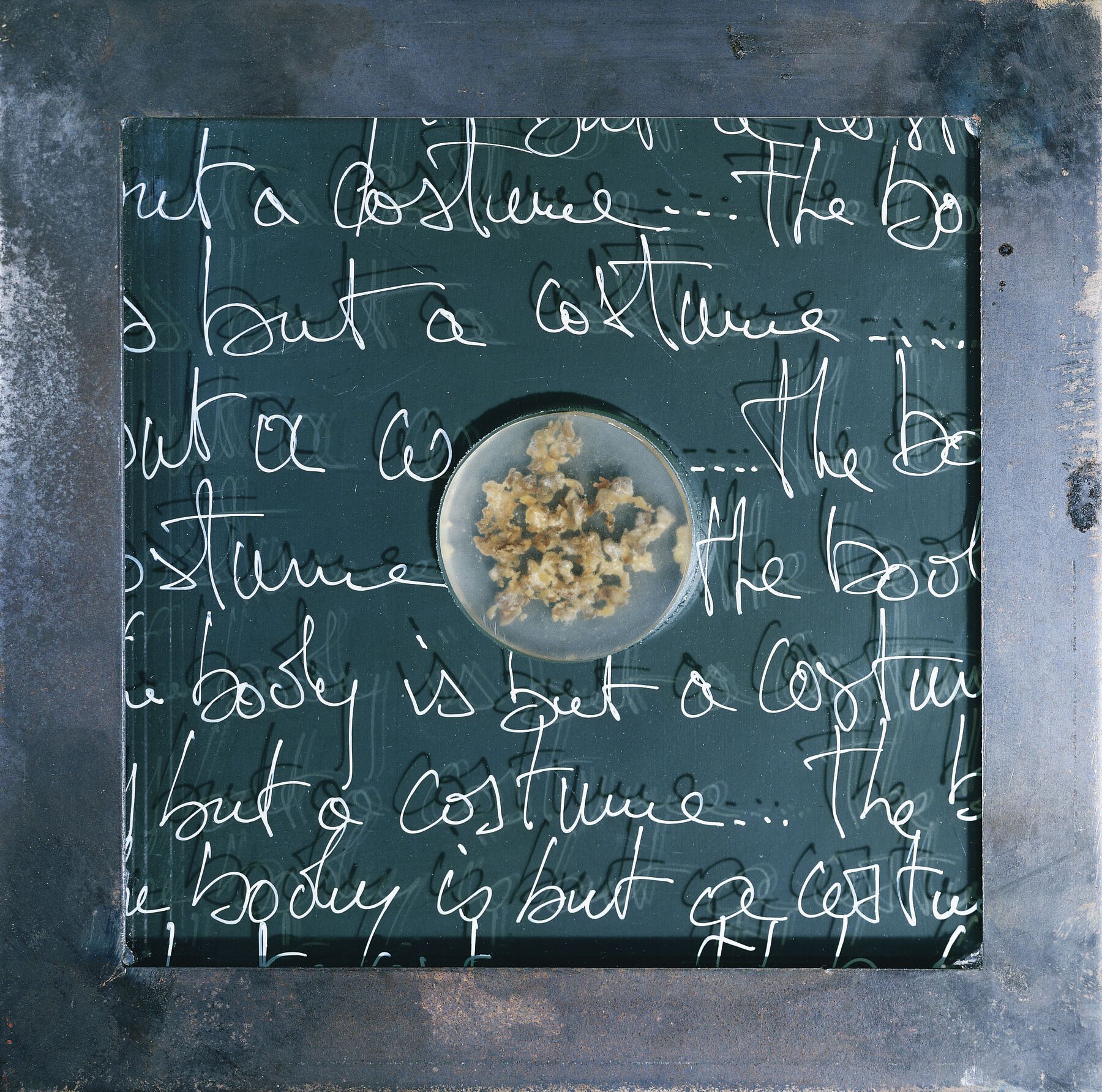 A petri dish with artist ORLAN’s skin tissues that are placed on top of a metal burglar-proof glass with white lettering in French