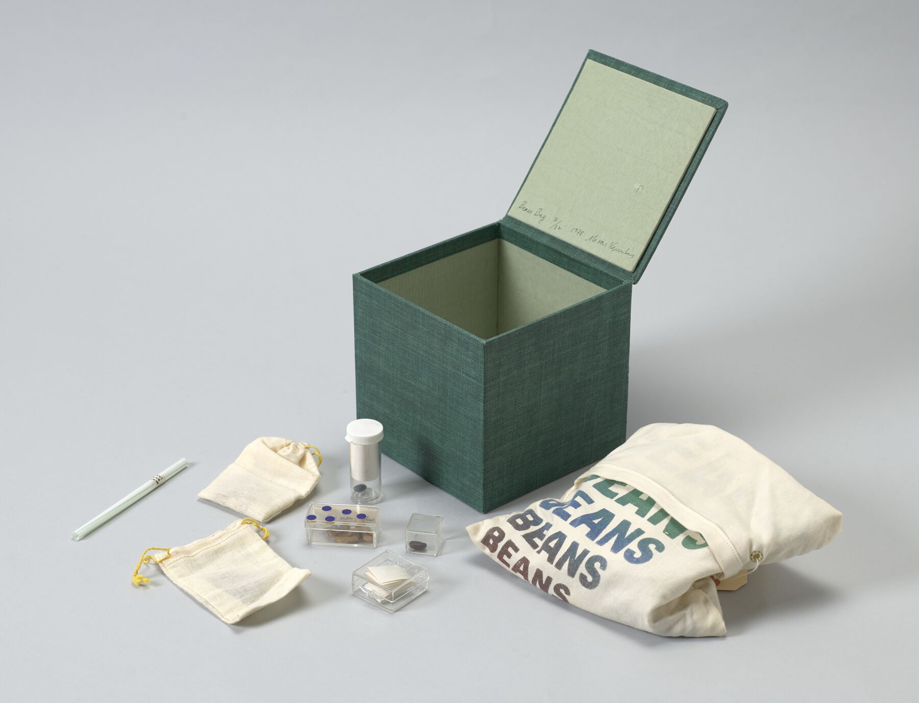 Assorted objects: white cloth bag printed with colorful text-lines reading ‘BEANS’; open green box; cloth pouches; glass cases