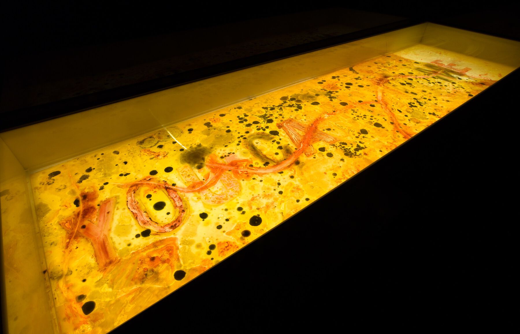 Depressed yellow luminescent plexiglass with black (or colored) spots, reading, “YOU [illegible] ME” in red clumpy material