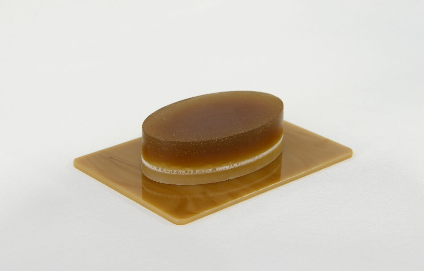 Yellow-gold ovular soap with thin white ring running around atop gold tray adjoining white wall