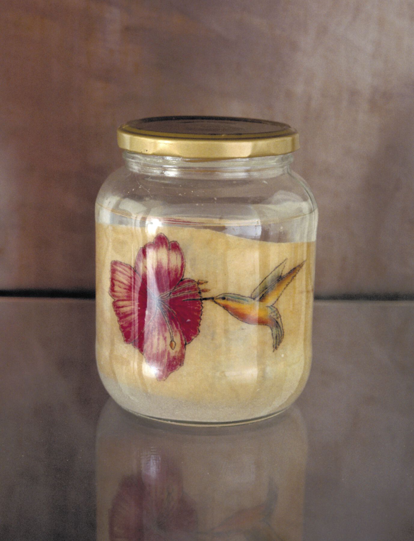 Glass jar holding fine tan dust with colorful imagery of hummingbird pointing beak into pink hibiscus flower