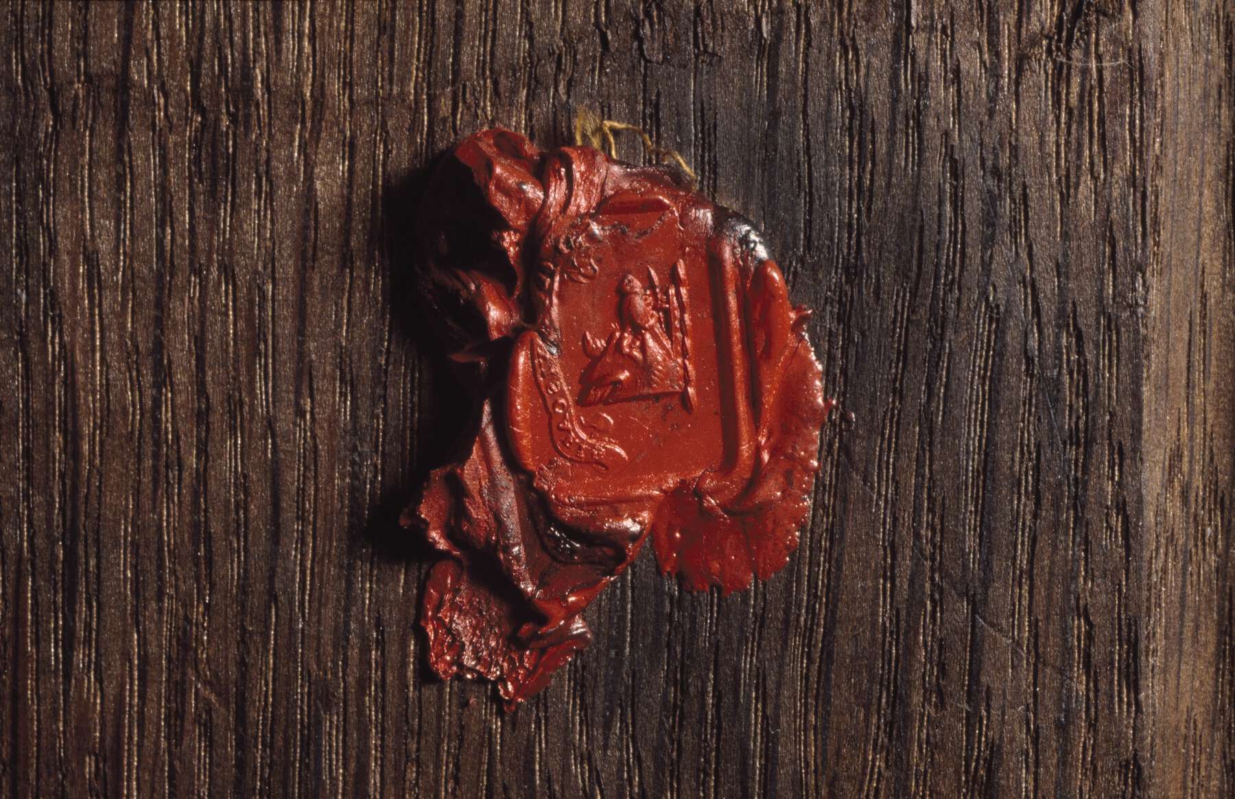 a reddish-orange wax seal with a stamp depicting a man on his knees