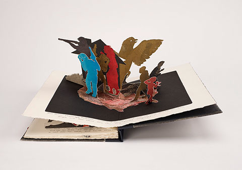 An open pop-up book displays a three-dimensional paper cutout of a scene featuring several human figures. 